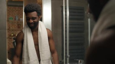 Afrika kökenli, etnik, sağlıklı bir adam, bir bardak su içer, ev banyosu yapar. Çıplak erkek, soğuk su içeceği içer, sağlık hizmetleri alışkanlığı dengeler. H2O ferahlatıcı, nemlendirici.