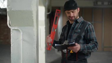 Kafkasyalı inşaatçı elinde cetvel tutarken düşünceli mühendis ustabaşı inşaat sahasına ölçümler yazarken tamirci adamın yenileme planı yazdığını düşünüyor.