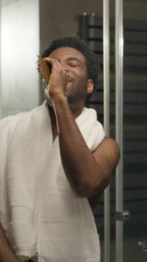 Komik adam, Afrikalı Amerikalı banyoda şarkı söylüyor, aynaya bakıyor, duş alıyor, mutlu, çıplak, erkek dans ediyor, saç fırçasında şarkı söylüyor, sağlıklı adam eğleniyor, müzik dinliyor, saç bakımını yapıyor.