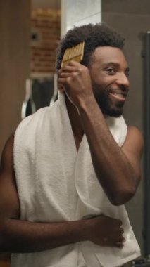 Banyodaki aynadaki yansıma saçına bakan Afrikalı Amerikalı adam gülümseyen etnik adam saç fırçası tarayan yakışıklı erkek, saç stili tarağı sabah güzellik şampuanı hazırlayan otel evindeki rutin şampuan kremi.