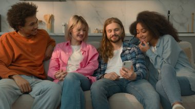 Kafkasyalı adam elinde cep telefonu tutarak sosyal medya sitesini çok ırklı insanlara gösteriyor. Çeşitli erkekler erkek Afrikalı Amerikalı kadınlar. Kanepede oturup konuşan kadınlar.