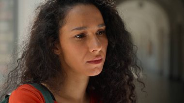 Üzgün, hayal kırıklığına uğramış, üzgün, bunalımlı, düşünceli, Latin bir kadının üniversite akademisi koridorunda öğrenim gördüğünü düşünen, sorunlu, eğitimli, zorbalık yapan Latin bir kız öğrenci.