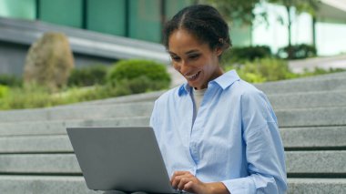 Mutlu gülümseme şaşkın Afrikalı Amerikalı kadın etnik iş kadını ofis dışında dizüstü bilgisayar yazıyor müşterilerle sohbet ediyor kadın iş kadını şehirli işkadını bilgisayar başında çalışıyor.