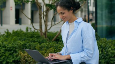 Mutlu gülümseyen Afro-Amerikan iş kadını şehirde dizüstü bilgisayar yazıyor. Ofis dışında müşterilerle sohbet ediyor. İnternet işçisi, iş kadını, iş kadını, şehirli, çalışan bilgisayar işvereni.
