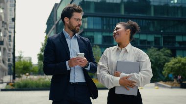 Şehirde çok ırklı iş adamları dolaşıyor Kafkasyalı iş adamı erkek Afrikalı kadın iş kadını kadın konuşmalar ofis bilgisayarında dizüstü bilgisayar tutuyorlar