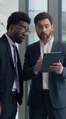 İki farklı etnik çeşitlilikte iş adamı dijital tablete bakarak online başarıyı tartışıyor. İyi haber, çok ırklı iş adamları ofiste yeni başlayan büyüme hakkında konuşuyorlar.