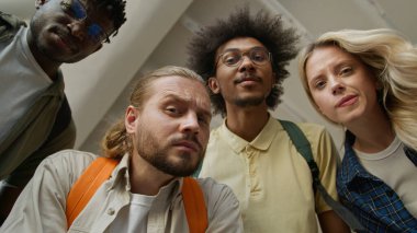 Bottom view Üniversitesi 4 öğrencisinin kafası karışmış. Şaşırmış, çok ırklı arkadaşları var. Erkek, beyaz, Afrikalı, Amerikalı erkek, kadın, kamera karşısında beklenmedik bir eğitime bakıyor.