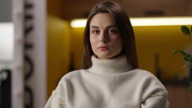 Ciddi bir beyaz kadın kameraya bakıyor. Evin içinde sakin bir bayan portresi kızı. Salondaki kadın portresi.