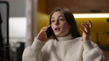 Beyaz kadın, el kol hareketleriyle konuşan, cep telefonlu, akıllı, cep telefonlu, cep telefonlu, duygusal bir kızı, oturma odasında, heyecanlı bir bayanla konuşuyor, içeride sohbet ediyor, arkadaşlarıyla iletişim kuruyor.