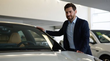 Beyaz adam müşteri alıcısı heyecan dolu erkek galerisini inceliyor. Yeni araba taşıma aracına dokunuyor. İş adamı satın alıyor.