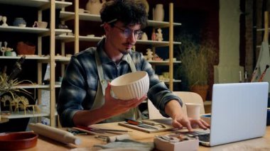 Kafkas erkek heykeltraş çömlekçi çevrimiçi laptop alışverişi çömlek atölyesinde el yapımı seramik küçük işletme sahibi satış sanatçısı erkek zanaatkar tasarımcı el işi çanak çanak çanak taşlı eşya satışı