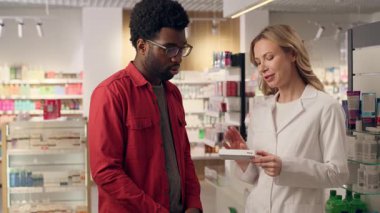 Eczacı, eczanede müşteri tıbbının Afrika kökenli Amerikalı erkek, beyaz kadın hapları almasına yardım ediyor. Vitaminler, ilaç, doktor, hasta bakımı, tıbbi danışmanlık, uzman ilaç uzmanları,