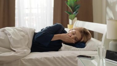 Uykucu Kafkasyalı kadın yatakta uyanıyor. Yatak odasında zamanı geçmiş cep telefonunu kontrol et. Şok olmuş bir kadın.