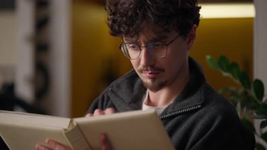 Düşünceli, ciddi, beyaz hippi adam evde kitap okumayı düşünüyor. Erkek okuyucu, klasik edebiyat roman sayfaları okuyor. Kapalı alanda ders çalışıyor.