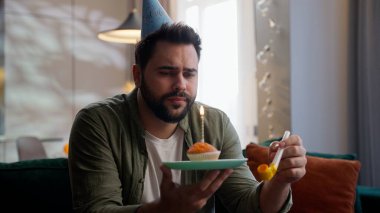 Bunalımlı, üzgün, umutsuz, Kafkasyalı iş adamı, iş adamı, ev sahibi, ev sahibi, kutlama şapkalı, tek başına doğum gününü kutlayan, tabağını elinde mumlu kek ile evde düdük çalan adam.