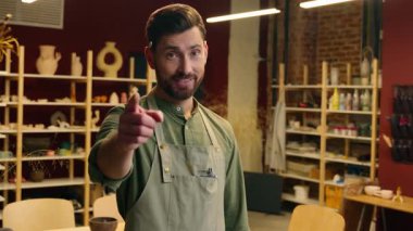 Neşeli gülümseyen beyaz adam, iş adamı, apron satıcısı, çömlekçi görünümlü küçük işletme sahibi, kameraman, işaret parmağıyla hoş geldin diyor.