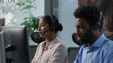 Çoklu etnik merkezli çağrı merkezi ekip çalışması Kafkas erkek amiri Afrikalı çağrı merkezi operatörü kulaklığı takıyor bilgisayar yardım hattında çalışan Hintli kadının başını sallıyor rehberlik eğitimi