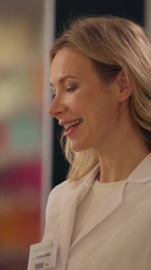 Sağlık çalışanı kadın eczacı eczanesinde konuşuyor. Eczanede tıbbi yardım alıyor. Müşteri ilaç paketini kasiyerden alıyor.