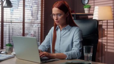 Ofiste dizüstü bilgisayarda çalışan beyaz iş kadını kameraya bakıyor. Durdurmak için el ele tutuşuyor. İşaret yok.