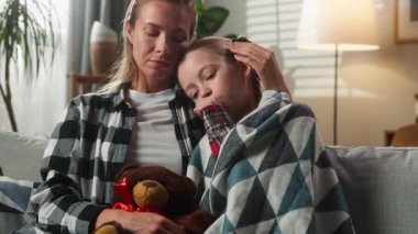 Kafkas ailesi evde sarılıp yatıyor hasta kızını teselli ediyor kanepeye örtünüp hasta öksürüyor üzgün çocuk kız Teddy Bear 'a sarılıyor öksürük şurubu hastalıklı sağlık sorunu