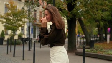 Beyaz tenli, mutlu, güler yüzlü, şehirde gezen, güneşli havanın tadını çıkaran, güneş gözlüğü takan, sokak lambasının etrafında dönen, şık iş kadınlarını kandırarak eğlenen bir kadın.