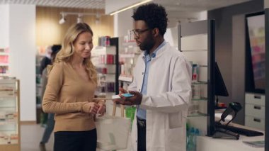 Afro-Amerikalı erkek eczacı, eczane doktorundan ilaç alan, ilaç siparişi veren, ilaç sipariş eden, ilaç alan, beyaz kadın müşterilere danışmanlık yapıyor.