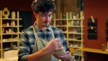 Beyaz tencereli çömlekçi elinde çanak çanak çömlek ürünü porselen el işi atölyede gülümseyen erkek heykeltraş tasarımcı seramik sanat eserleri gösteren küçük işletme sahibi.