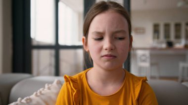 Kızgın küçük Kafkasyalı çocuk kanepeye vuruyor. Kötü davranışları yüzünden evde cezalandırılıyor. Kız çocuğu kollarını kavuşturuyor.