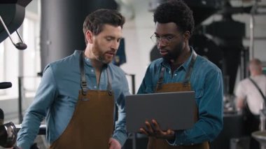 Kahve teftişi. İki Afrikalı barista uzmanı dizüstü bilgisayar tutuyor. Kafkasyalı meslektaşı, aroma aromalı kızartma makinesini inceliyor.