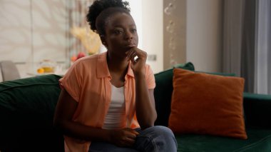 Düşünceli, düşünceli, Afro-Amerikalı iş kadını, kadın iş kadını, ev sahibi, kanepe sahibi derin düşüncelere dalıp evdeki oturma odasında şüpheli bir karar vermeyi düşünüyorum.