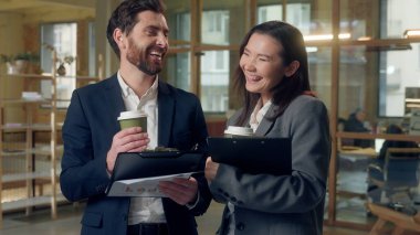 Çok uluslu gevşek iş ortakları ellerinde kahve tutan belgeleri tartışıyor Koreli iş kadını Kafkasyalı iş adamı mutlu takım çalışması pano ofis işi fikri kırma stratejisi raporu