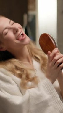 Kafkasyalı mutlu bir kadın model banyodaki kadın bornoz dansında saçlarını tarayıp şarkı söylüyor. Mikrofon şarkıcısı taklidi yapıyor. Komik saç stili.