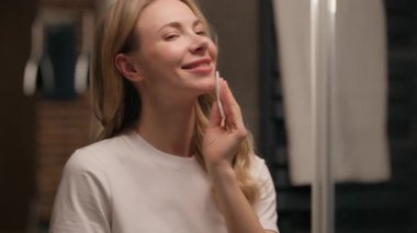 Mutlu kadın aynaya bakıyor pamuk pedi tutuyor yüzünü temizliyor banyoda sağlıklı cilt Kafkasyalı güzel bayan makyaj yapıyor yumuşak nemlendirilmiş yüz bakımı cilt bakımı