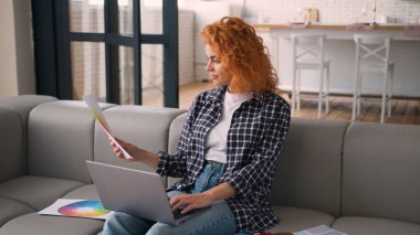 Kanepede oturan beyaz kadın ev sahibi ile meşgul dizüstü bilgisayar kullanıyor yenilenme için bilgisayar alıyor renk paleti seçiyor renkli şablon ev tasarımı yapıyor.