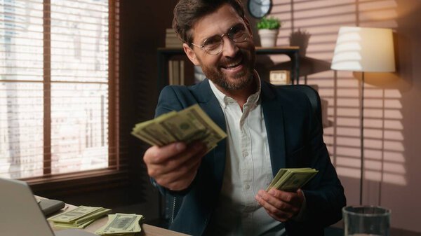 Богатый кавказский инвестор среднего возраста бизнесмен мужчина в офисе, подсчитывающий денежные доходы от заработной платы, глядя в камеру улыбаясь давая деньги предложение инвестиционного банка пари казино