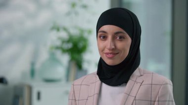 Ofisteki mutlu, gülümseyen, dişlek, etnik Müslüman iş kadını, kameraya bakan, gamsız, Hintli, İslamcı iş kadını, tesettürlü, tesettürlü bir kadın olarak poz vermekten memnun.