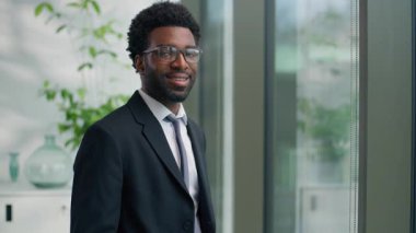 Afro-Amerikalı iş adamı, pencereye bakan erkek işadamı, ofis yöneticisi şirket CEO 'sunun kamera portresine gülümseyen, kapalı alanda başarılı etnik girişimci gülümsemesi.