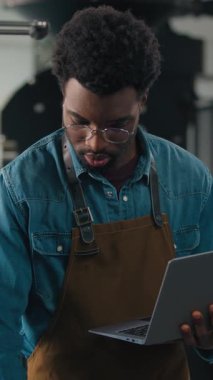 Afro-Amerikalı etnik erkek adam kahve endüstrisi uzmanı taze kavrulmuş fasulye daktilo dizüstü bilgisayarını kontrol ediyor. Gidiyor. Müfettiş, kızartma makinesi kalitesinde rostoyu küçük işletmelerle birlikte inceleyin.