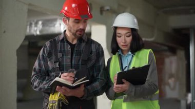 Çok uluslu ciddi mühendisler inşaat çözümlerini tartışıyorlar. Asyalı kadın değerlendirmesi için kararları tartışıyorlar. Kafkasyalı erkek not defteri yazıyor. Takım çalışması altyapı yenileme stratejisi.