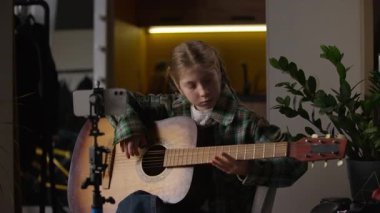 Küçük beyaz kız gitar çalmayı öğreniyor. Evde ders çalışıyor. Okul çocuğu blogcu çocuk müzik enstrümanı çalıyor.
