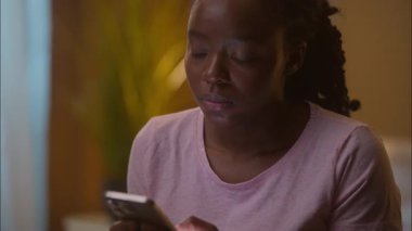 Üzgün, düşünceli, düşünceli, Afrikalı, Amerikalı, etnik kadın kız. Uyutma aleti bağımlılığı ruhsal bunalımından önce cep telefonuyla sosyal medyayı karıştırıyor.