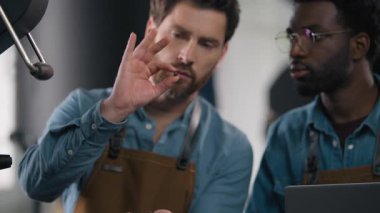 Çok ırklı kahve fabrikası işçileri Afrikalı Kafkasyalı erkekler kavrulmuş tohum kokusu değerlendirme içeceği uzmanlığı ellerinde fasulye espresso kaliteli küçük işletme imalatı.