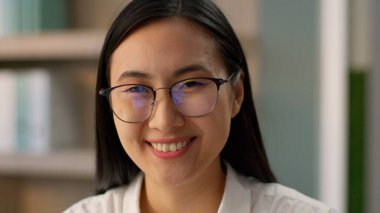 Yakın plan mutlu Asyalı Asyalı iş kadını kadın yönetici gülümseyen Çinli Koreli iş kadını kadın işçi sekreter işveren gözlüklü ofis kamerasına bakıyor.