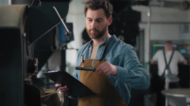Kafkasyalı adam kahve aromalı fasulye kızartma makinası ekipman uzmanı teknoloji uzmanı sektörü teftiş ediyor kafein kavurucu erkek adam not yazıyor kalite kontrol fabrikasına git