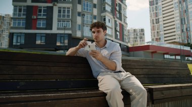 Kafkasyalı bir gencin elinde bir fincan kahve, cep telefonu, akıllı telefon, şehirli şaşkın adam, kötü haber, internetteki kötü haber, kafası karışmış, afallamış iş adamı.