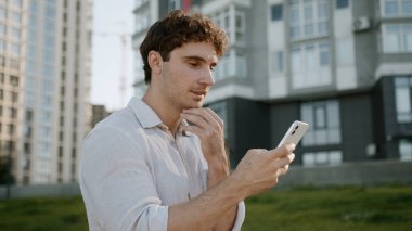 Kafkasyalı bir adam cep telefonu kullanıyor, akıllı telefon kullanıyor, sosyal medyada sohbet ediyor, internet üzerinden sohbet ediyor, gülümsüyor, uygulama yapıyor, erkek öğrenci aletleri, iş dünyası işadamı sokakta yürüyor, şehir dışına çıkıyor.