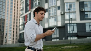 Kafkasyalı bir adam cep telefonu işini açık havada geziyor internet bağlantıları kuruyor uygulamalı erkek işadamı sohbet ediyor akıllı telefon, internet, sosyal medya işvereni profesyonel cihaz yürüyüşü