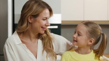 Mutfaktaki beyaz mutlu aile pozitif çocuk kızının kameraya sarılmasına gülümsüyor. Evlat edinilmiş sevimli kız kucaklaşması olan yetişkin bekar bir anne. Tatlı sevgi portresi yüzlerinin tadını çıkar.