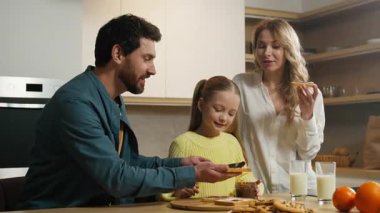 Mutlu bir gülümseme, beyaz bir aile, mutfakta, küçük kızlarıyla birlikte kahvaltı hazırlıyorlar. Çikolatalı sandviç yiyorlar. Anne, küçük kız, organik gıda marketi teslimatı.