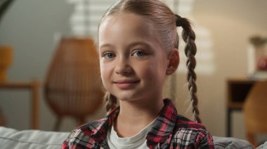 Kafkasyalı küçük kız çocuğunun portre yüzünü kapatın. Dertsiz tasasız, sakin, gülümseyen çocuk okul kızı. Evdeki çocuk esirgeme kurumundaki kanepede pozitifken kameraya bakıyor.